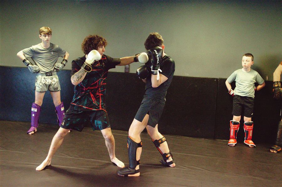 Two Warrior fighters exchanging in padded sparring while teammates watch